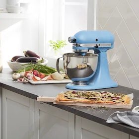 Light blue stand mixer on kitchen counter with fresh vegetables and flatbread