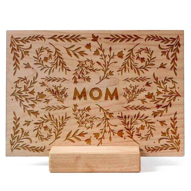 Wooden card with the word “MOM” engraved in the center, surrounded by floral and leaf patterns