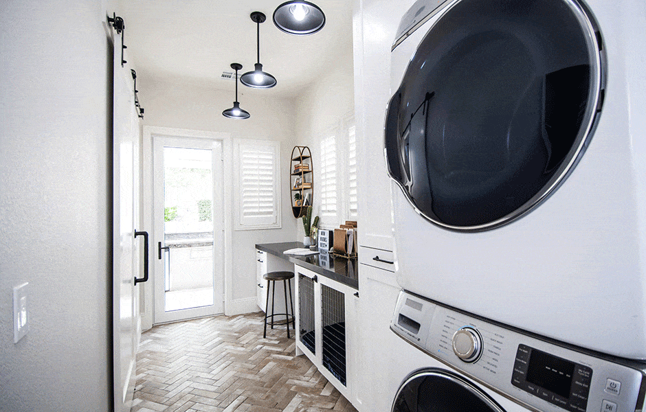 Bright laundry room with stacked washer and dryer, black countertops, pendant lights, and herringbone tile floor