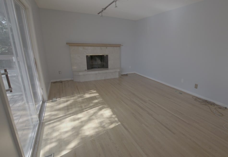 Empty living room with light wood floors, gray walls, a sliding glass door, and a simple fireplace