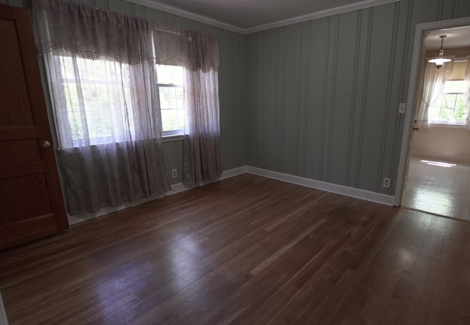 Empty room with wood floors, striped green walls, and sheer curtains