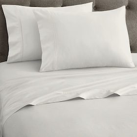 White bed sheet set with two matching pillowcases neatly arranged on a bed with a tufted gray headboard