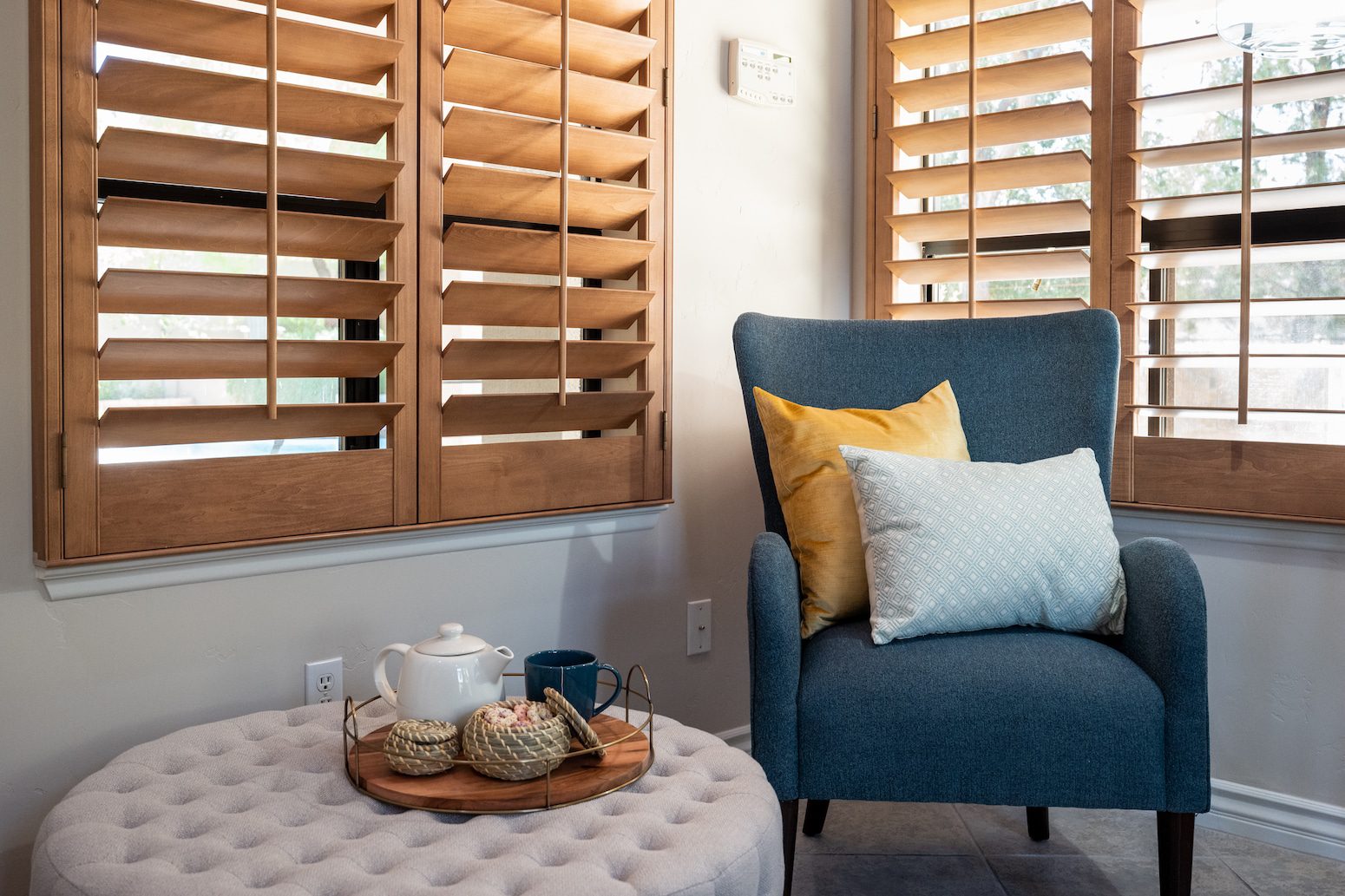 Cozy nook with blue chair, pillows, wooden shutters, and tea set