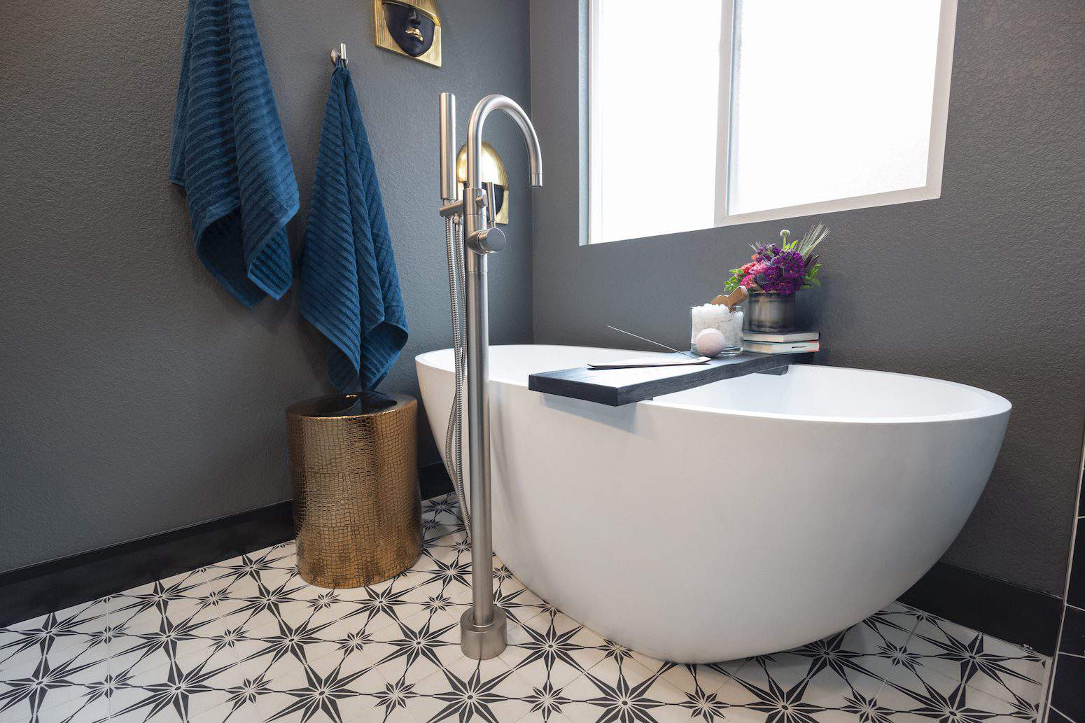 Modern bathroom with white tub, patterned tiles, gray walls, and blue towels