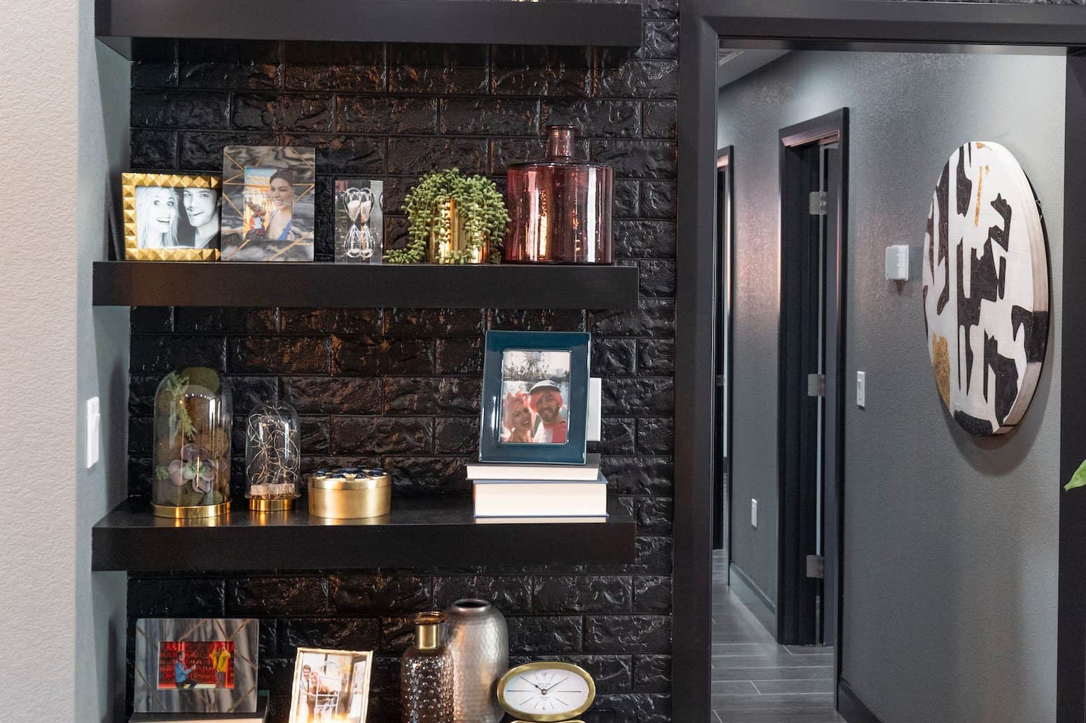 Modern black accent wall with floating shelves decorated with framed photos, vases, and small plants