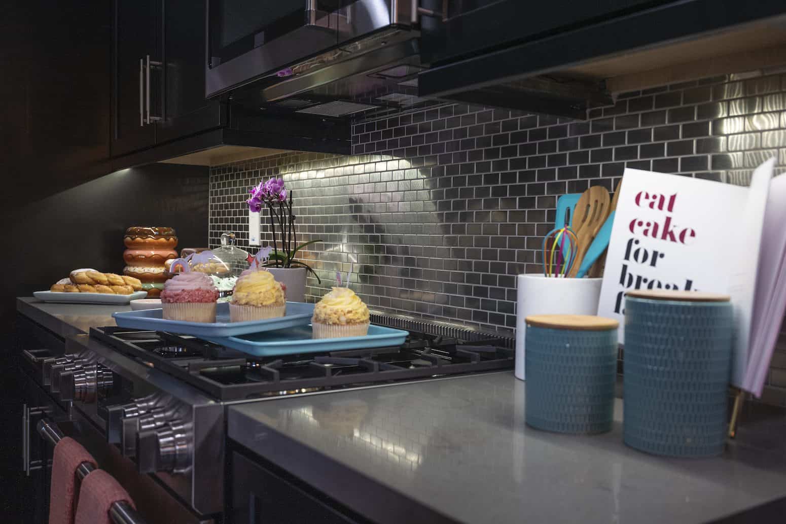 Kitchen with dark cabinets, stainless backsplash, cupcakes, and decor