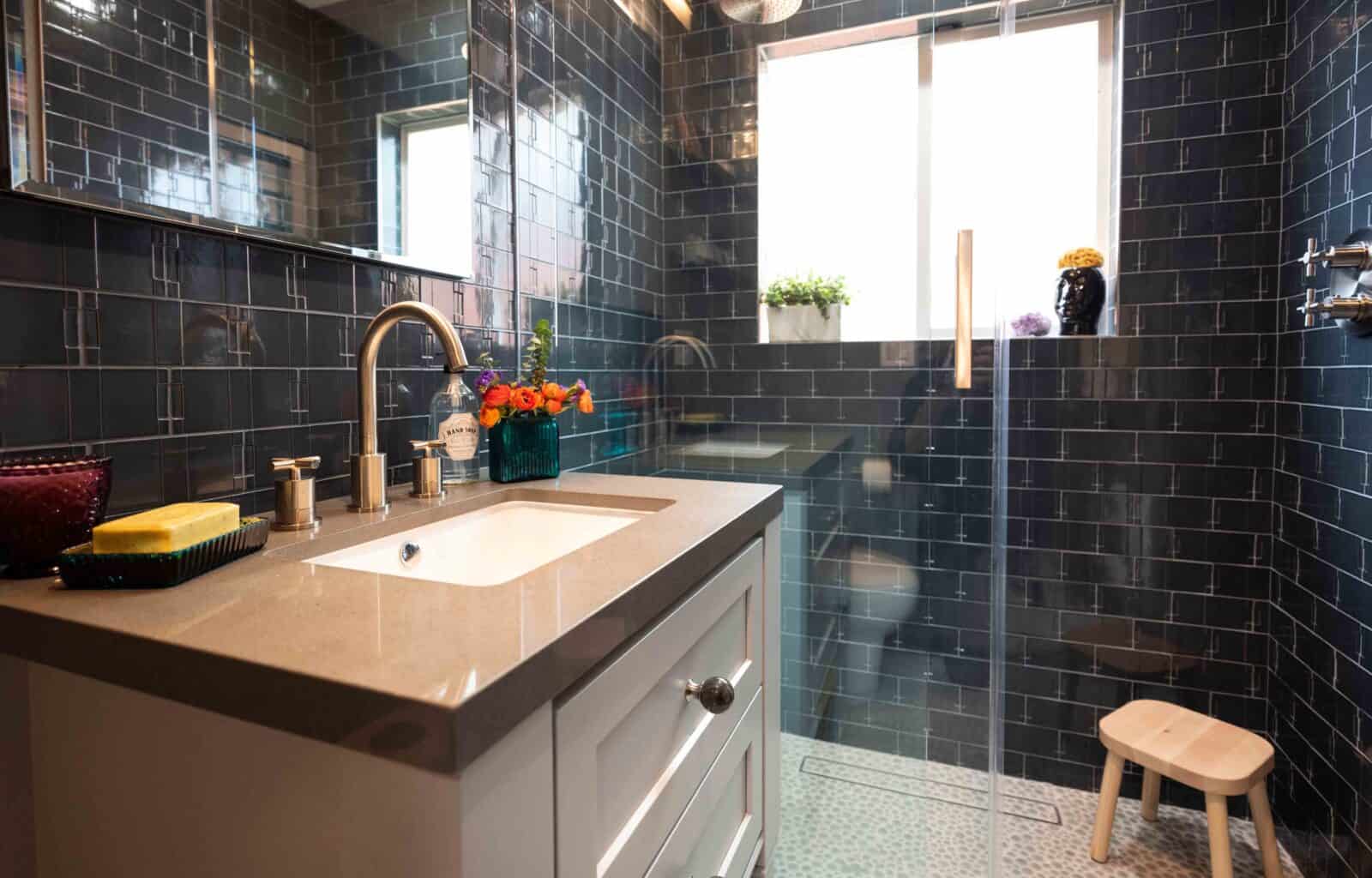 Modern bathroom with dark tiles, glass shower, and beige vanity