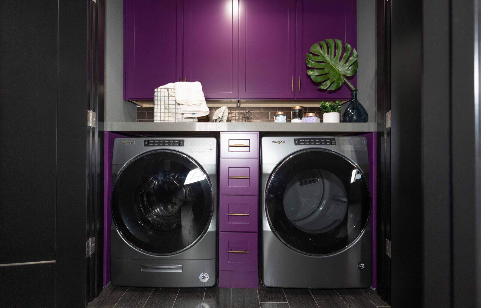Compact laundry nook with front-load washer and dryer, bold purple cabinetry, and a sleek countertop