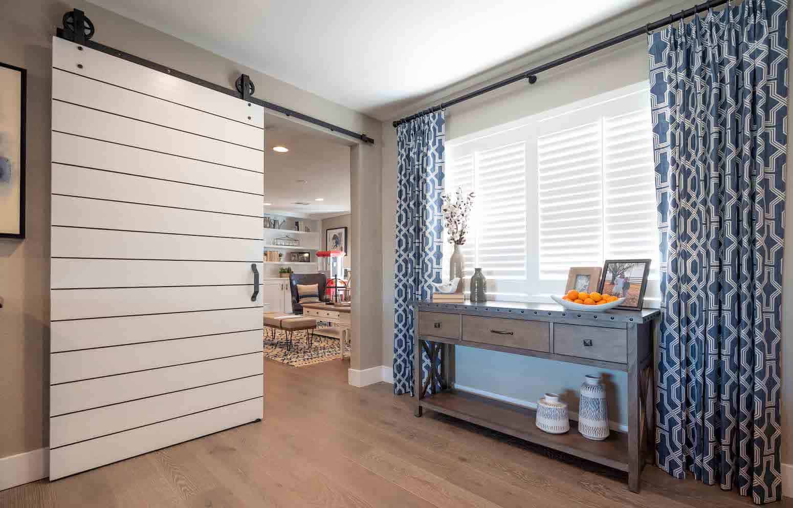Bright hallway with sliding white barn door, patterned blue curtains, and a console table with decor