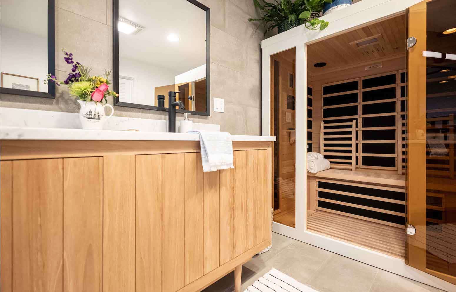Modern bathroom with a wooden vanity, black fixtures, a large mirror, and an infrared sauna with a glass door