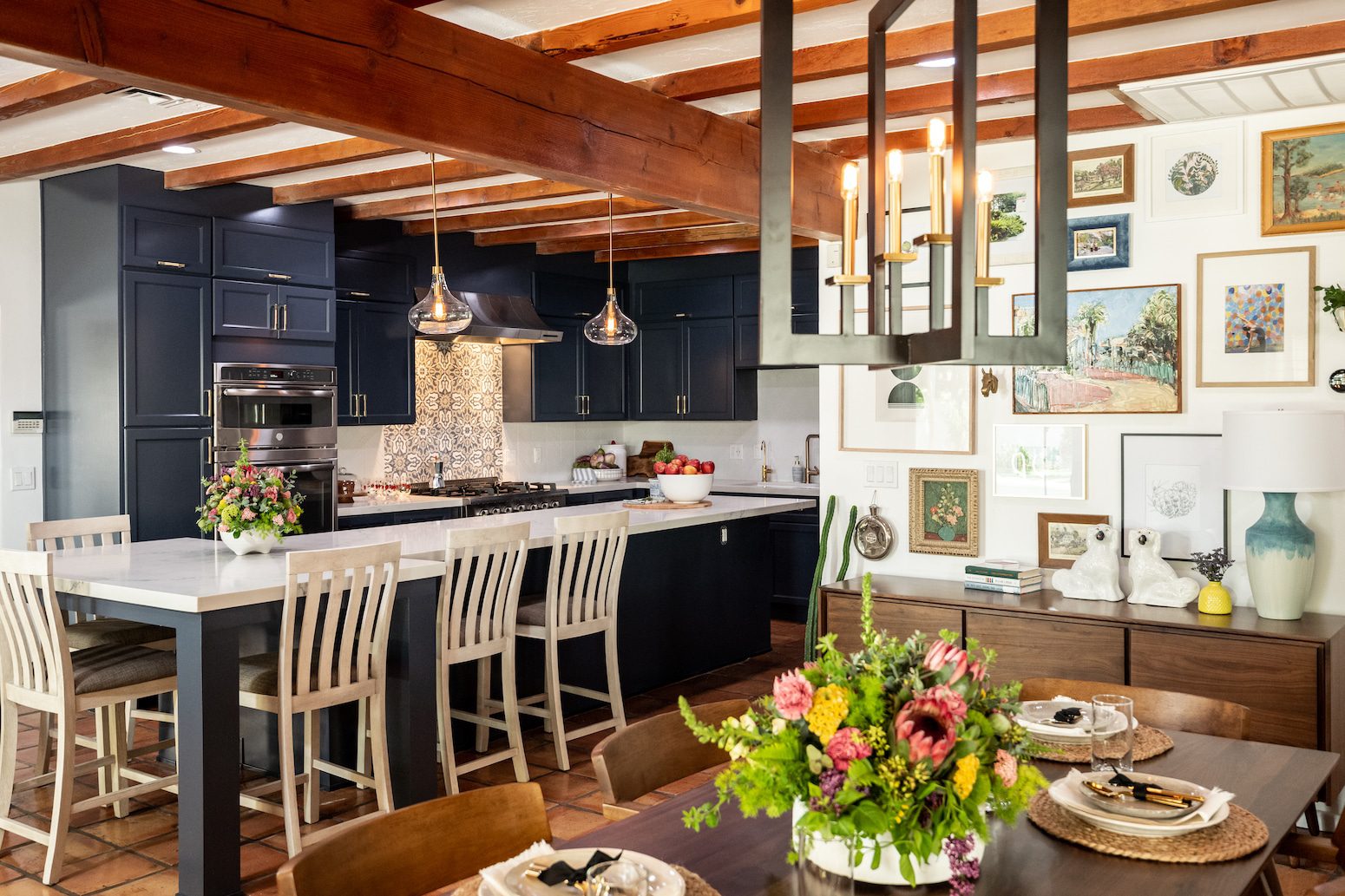 Exposed beams, navy cabinets, floral decor, and gallery wall in kitchen-dining space