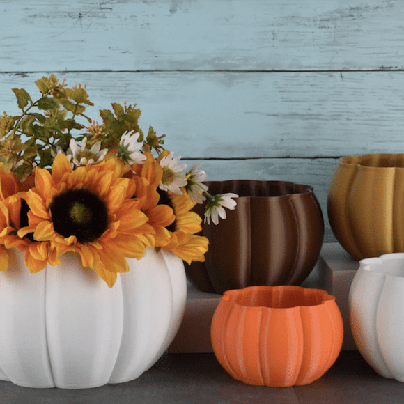 Pumpkin-shaped planters with fall floral arrangement against rustic wooden background