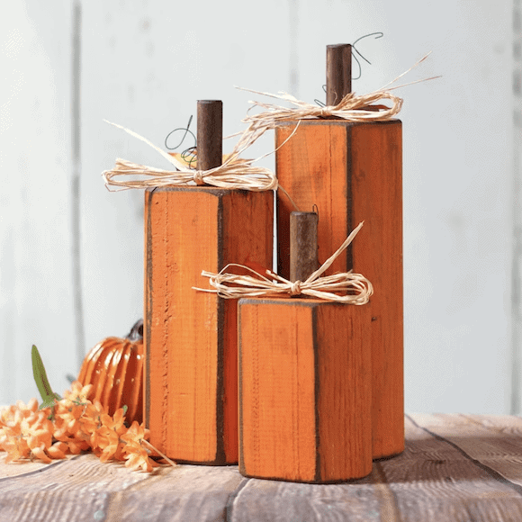 Set of three rustic wooden pumpkin decorations painted orange with brown stems and raffia bows