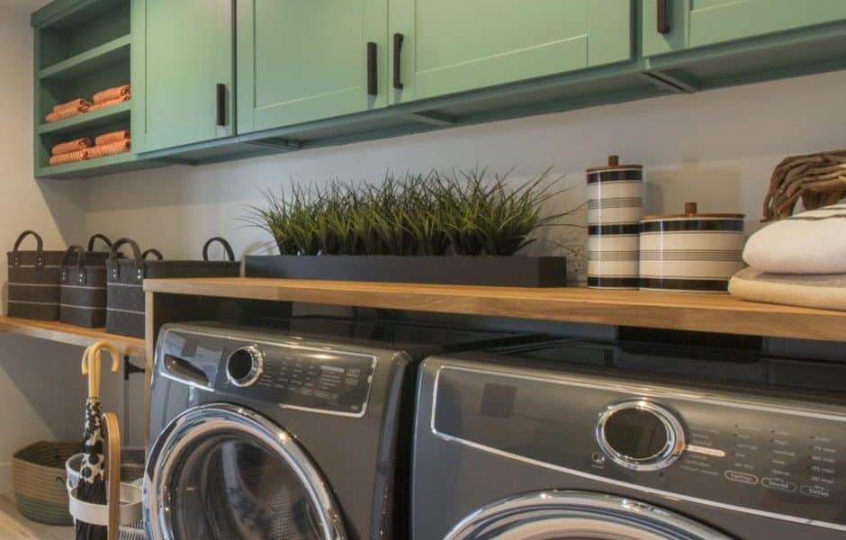 Modern laundry room with front-load washer and dryer, green upper cabinets, wood shelf, and decorative storage items