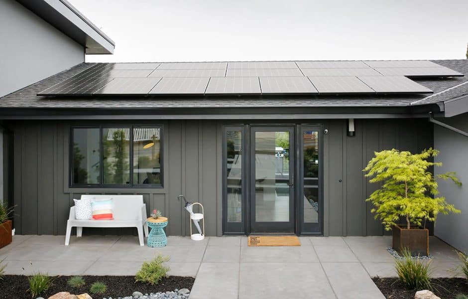 Modern house exterior with solar panels, black siding, and a small bench on the patio
