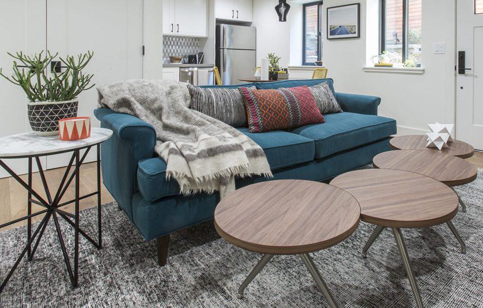 Modern living room with a teal sofa, patterned pillows, and round wooden tables