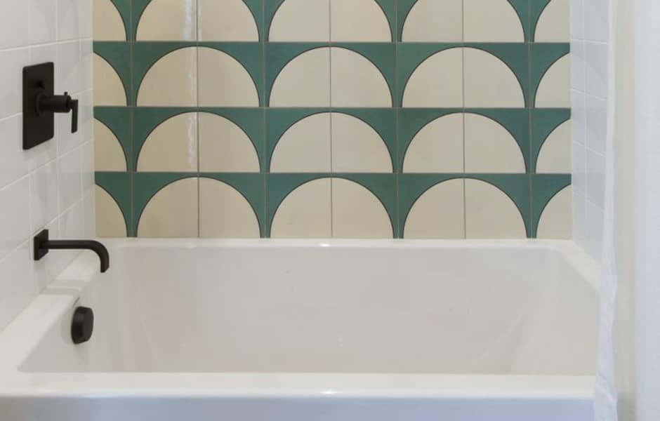Bathroom tub with geometric green and cream tile backsplash and black fixtures