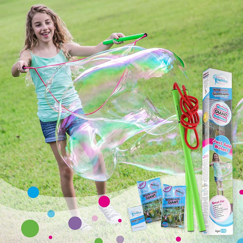 Girl using a giant bubble kit with green wands and bubble packaging in the background