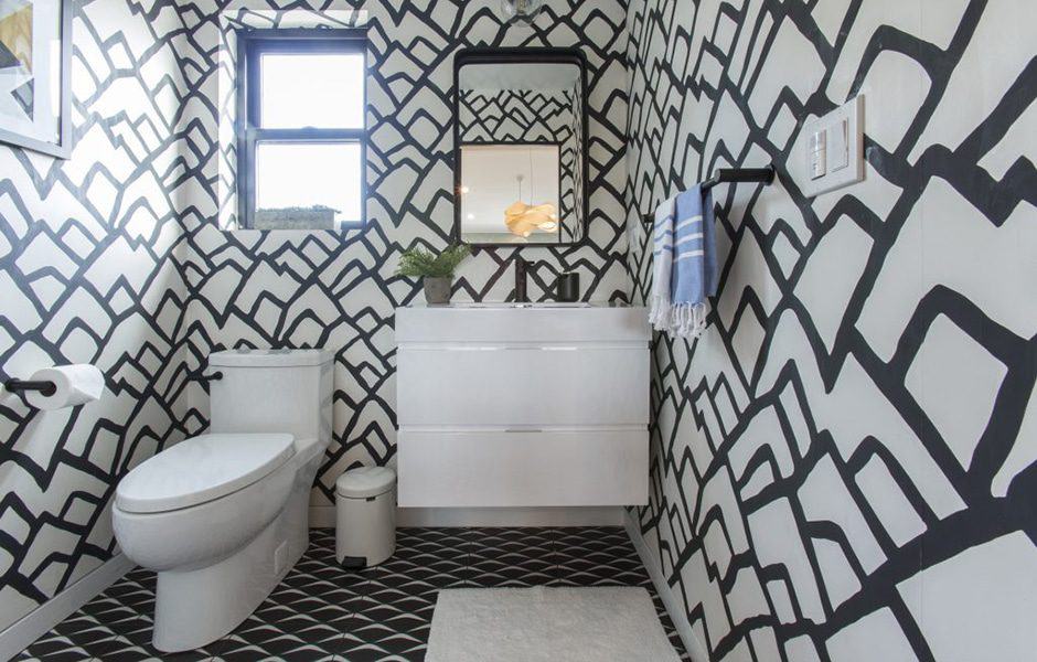 Modern bathroom with bold black-and-white patterned walls, a white vanity, mirror, and a toilet