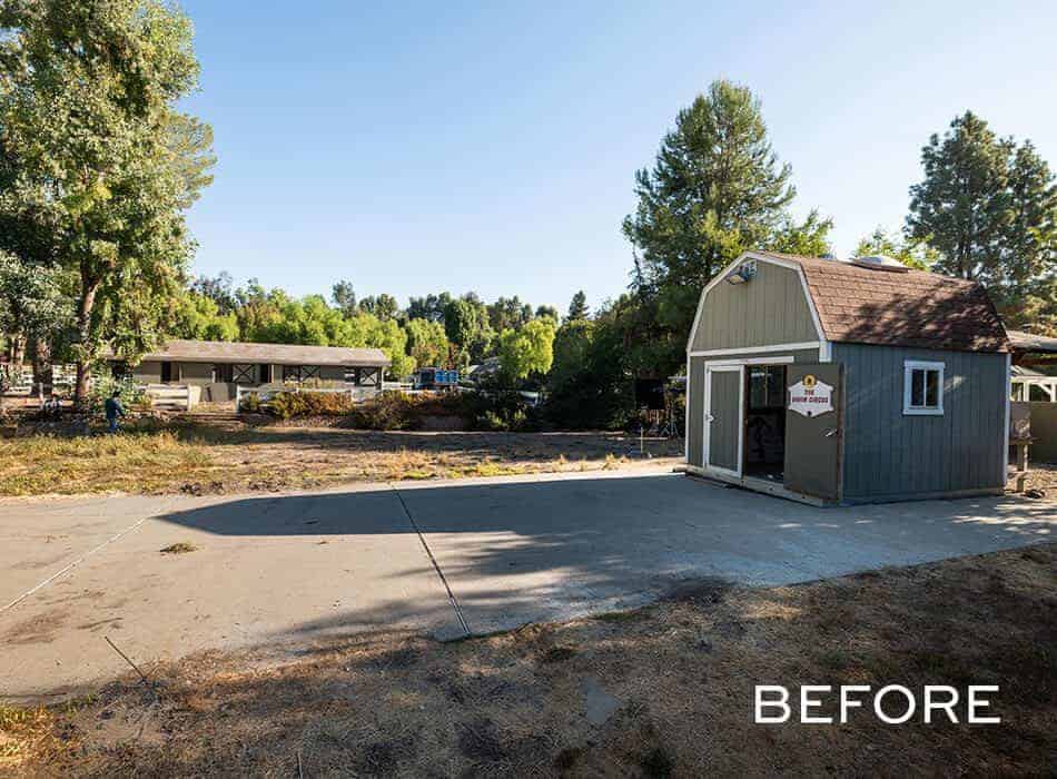 Gray barn-style shed on concrete driveway surrounded by trees