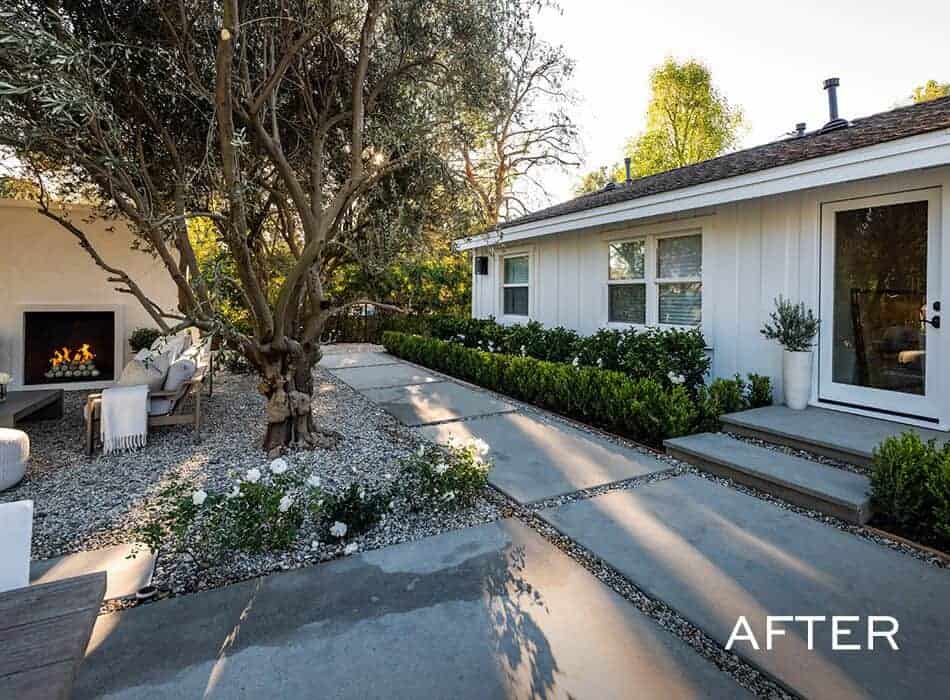 Modern backyard with concrete pathways, gravel landscaping, central tree, and outdoor seating by a fireplace