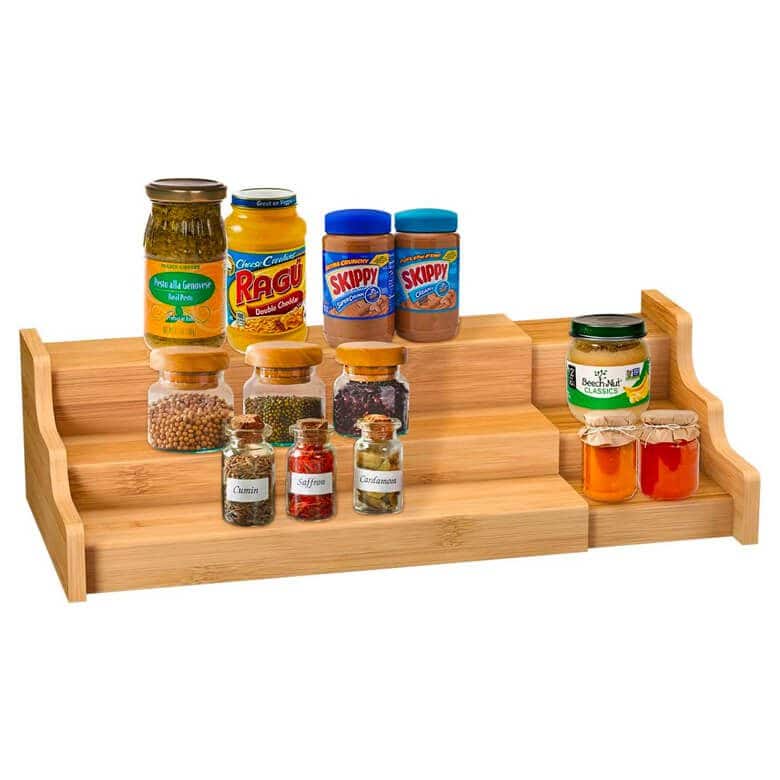 Three-tier wooden spice rack holding jars of spices, peanut butter, sauces, and condiments
