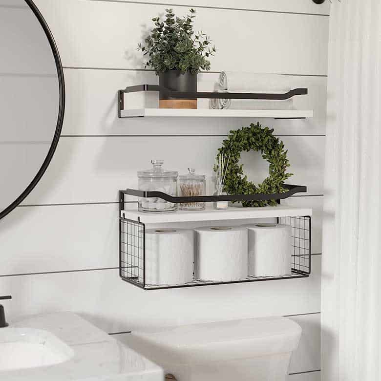 Bathroom wall shelves with black metal frames holding plants, jars, and toilet paper rolls above a toilet