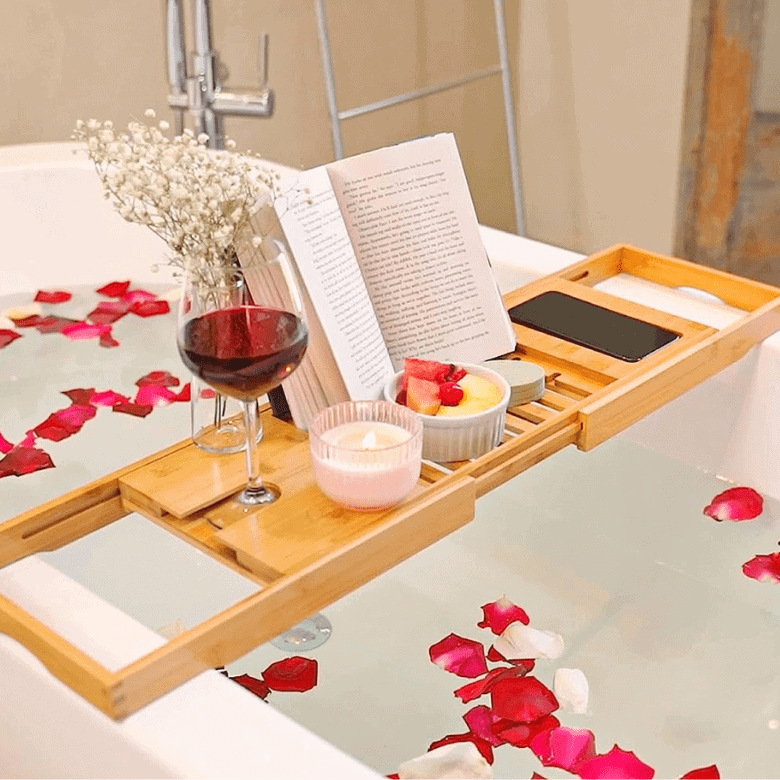 Bathtub with bamboo tray, book, wine, candle, snacks, and rose petals