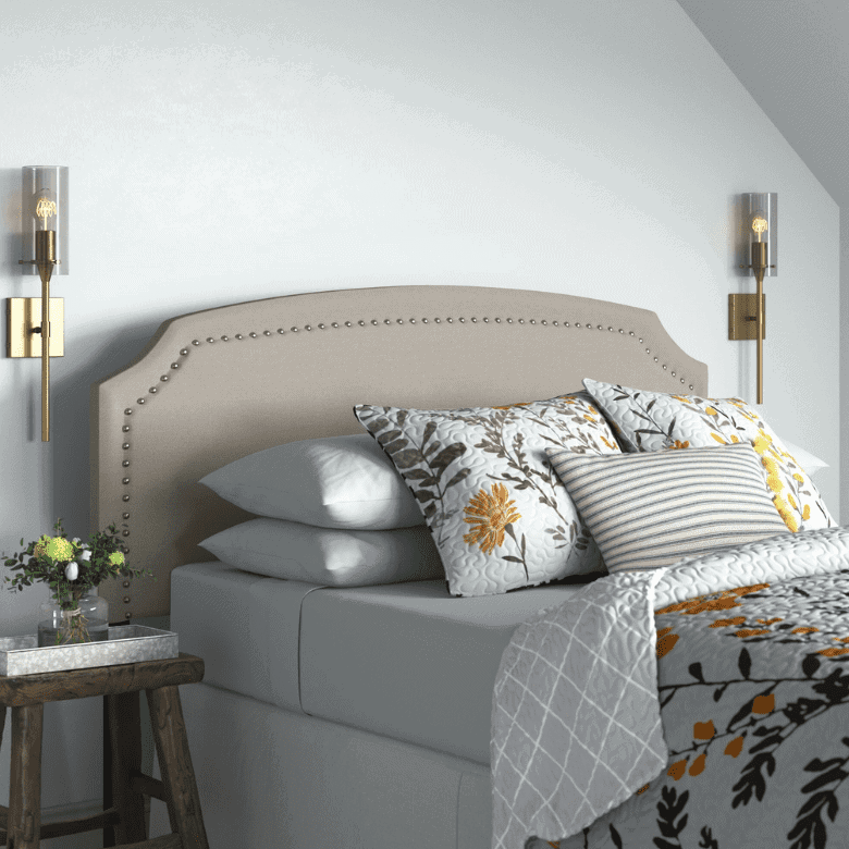 Bed with beige upholstered headboard, floral bedding, and wall-mounted sconces