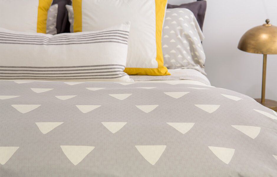 Modern bed with gray and white triangle-patterned bedding, accented by striped and yellow pillows