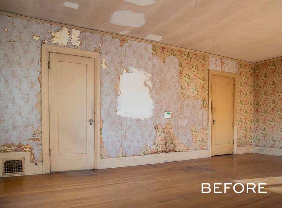 Room with peeling wallpaper, patchy walls, and two closed beige doors on a hardwood floor