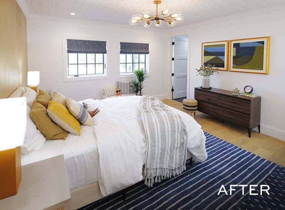 Modern bedroom with white walls, large bed with layered pillows, navy striped rug, and wooden dresser
