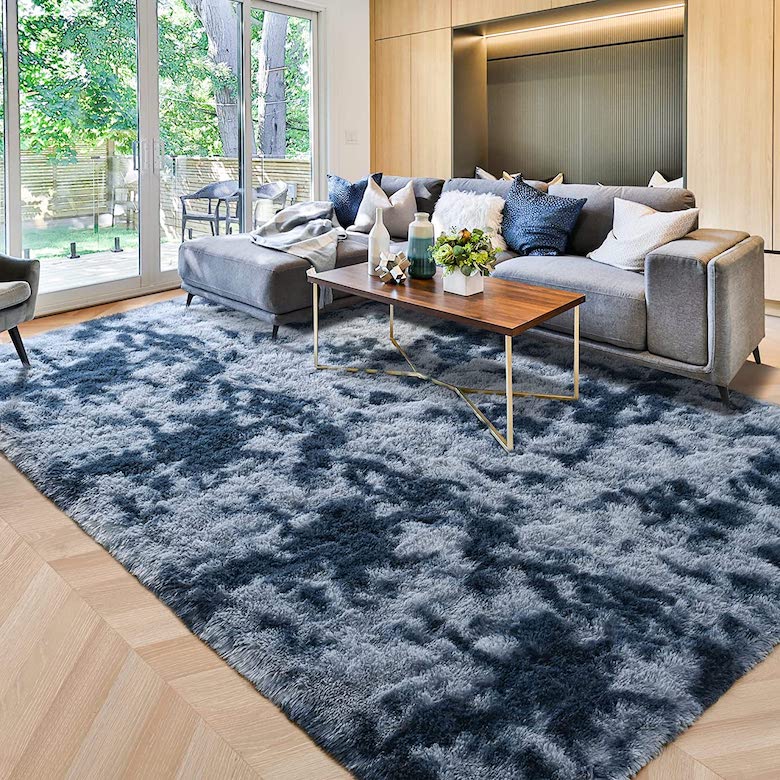 A gray sofa with pillows and a coffee table, positioned on top of the blue rug