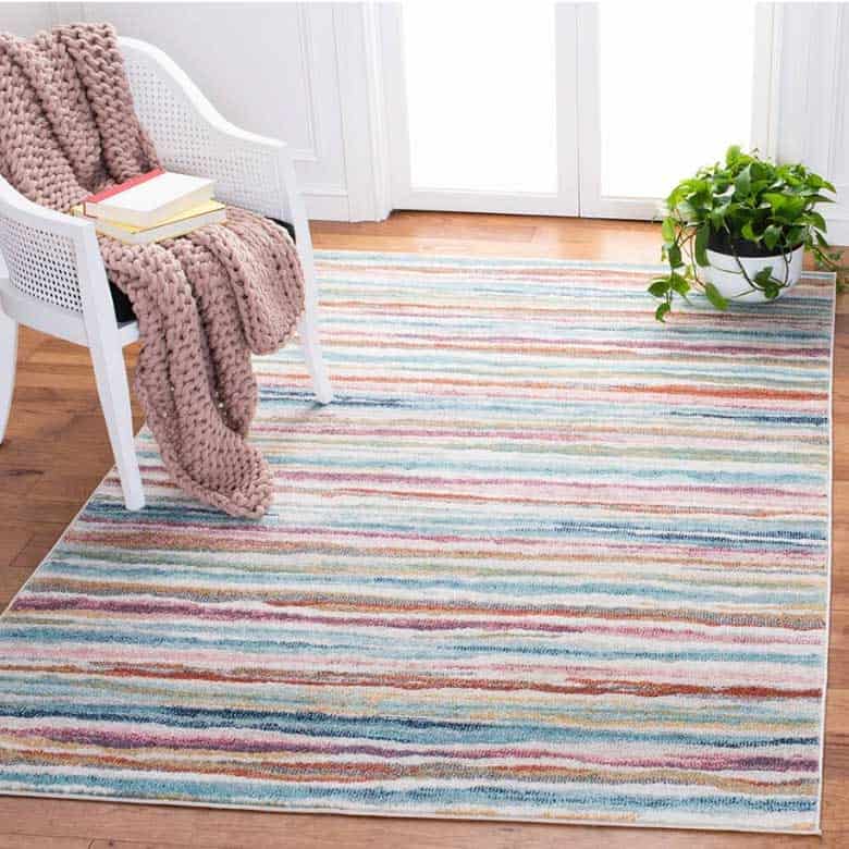 Striped multicolor rug with white chair, pink knit throw, and potted plant
