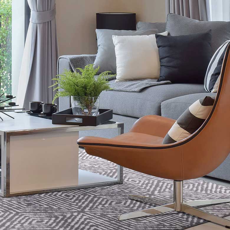 Living room with gray sofa, leather accent chair, geometric rug, and white coffee table