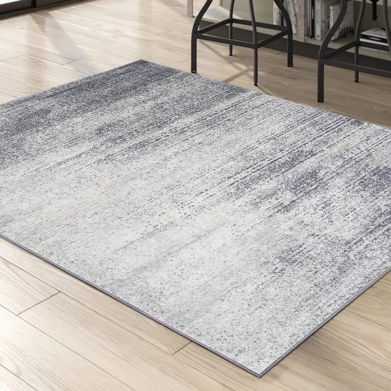 Gray gradient rug on light wood floor near black metal chairs