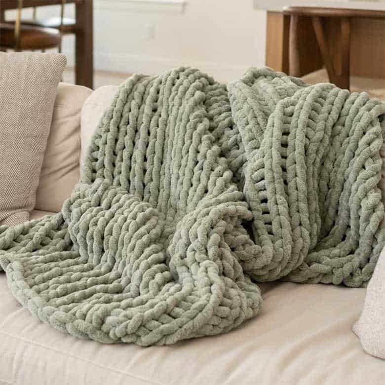 Chunky knit sage green throw blanket on a cream couch