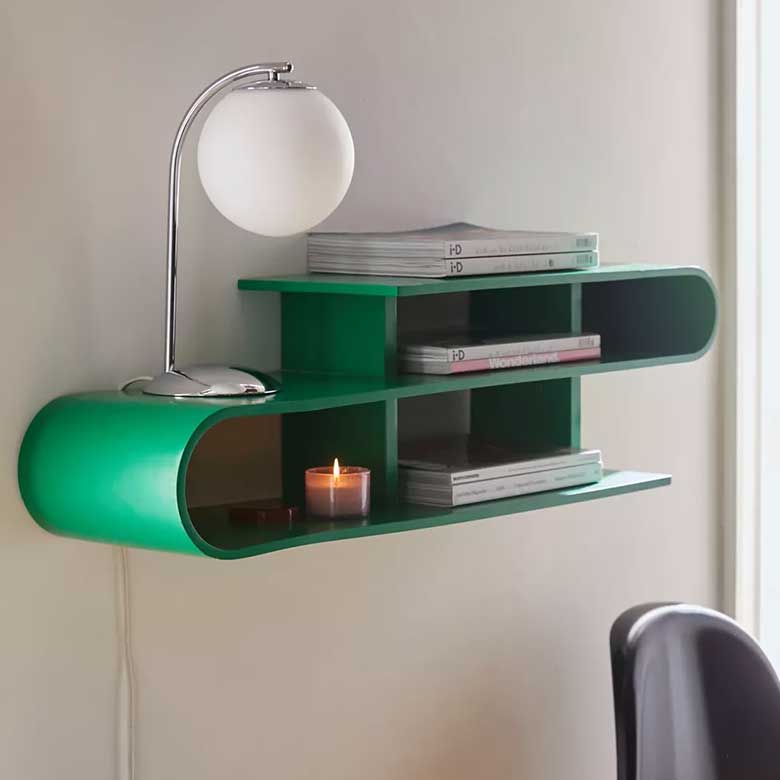 Green wall shelf with a table lamp, stacked magazines, and a lit candle