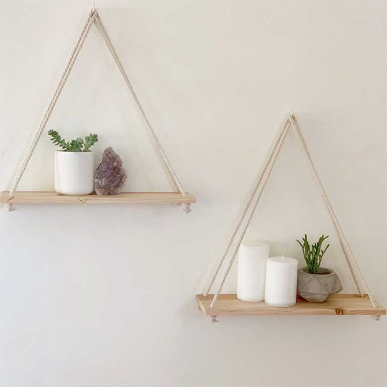Hanging wooden shelves with small plants, candles, and a crystal on a white wall