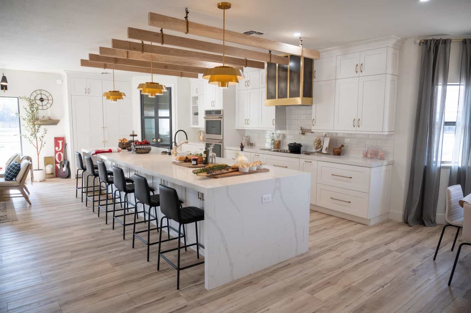 Bright kitchen with a large white island, gold pendant lights, and wood beam accents