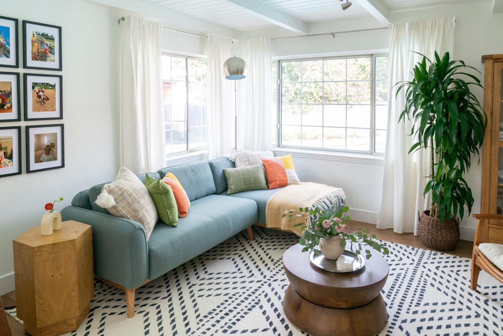 Bright living room with a blue sectional sofa, colorful pillows, large windows, and a patterned rug