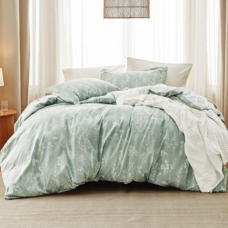 Soft green floral bedding with white pillows and cozy throws in a serene, light-filled bedroom