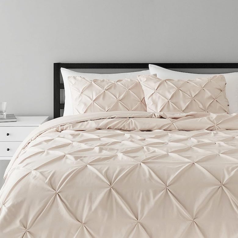 Beige pintuck comforter set on a bed with matching pillows and a black headboard