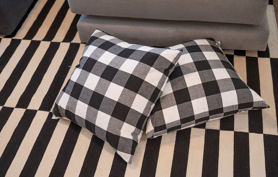 Two black and white buffalo check pillows resting on a striped rug