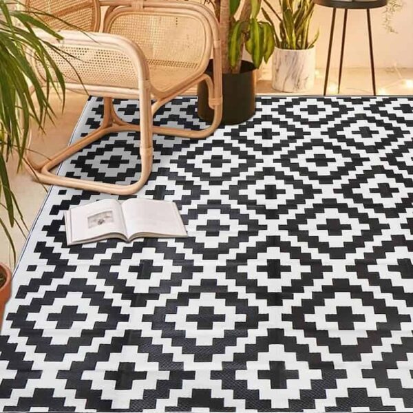 Black and white geometric patterned rug in a room with rattan chairs, potted plants, and an open book on the floor