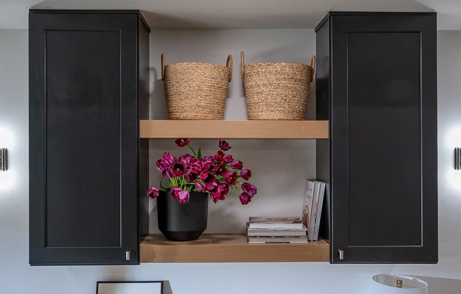Black cabinets with a wooden shelf displaying baskets, books, and a vase of purple flowers