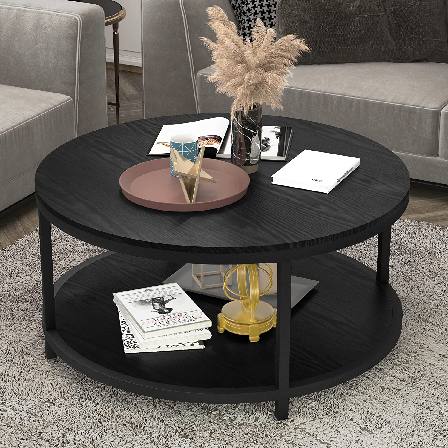 Round black coffee table with lower shelf, decorated with books, a vase, and decorative objects