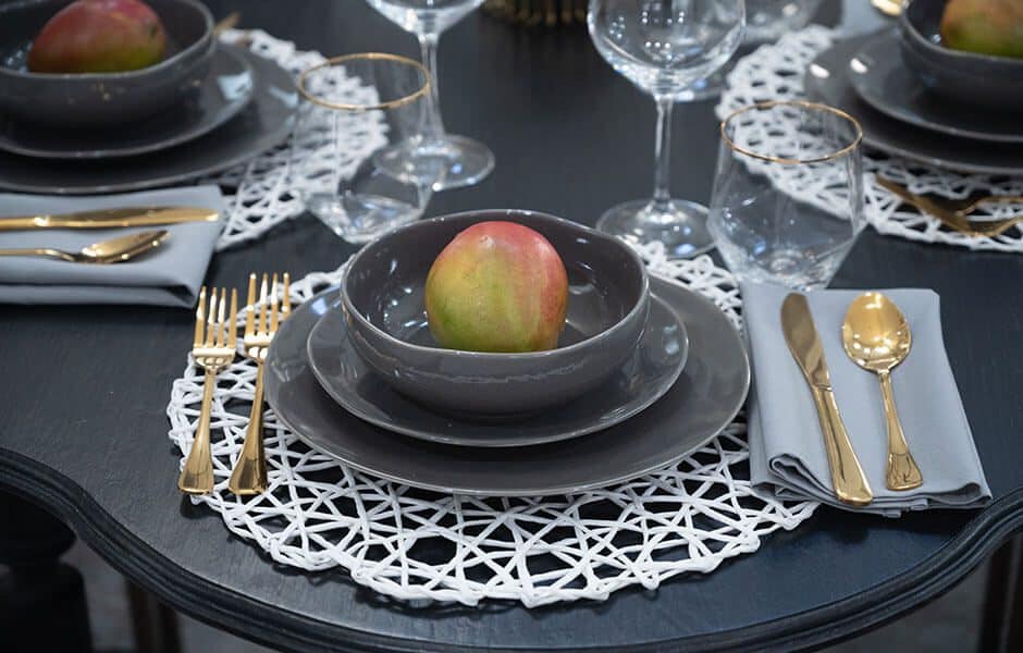 Elegant dining setup with gray plates, gold utensils, glassware, and a fruit centerpiece