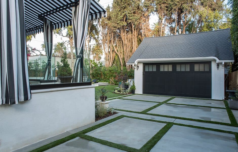 Modern outdoor space with striped awning and garage with concrete pavers and greenery