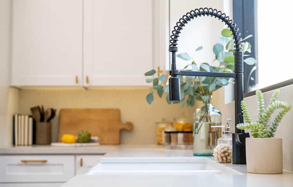 kitchen sink with a black spring faucet, white countertops, and decorative greenery